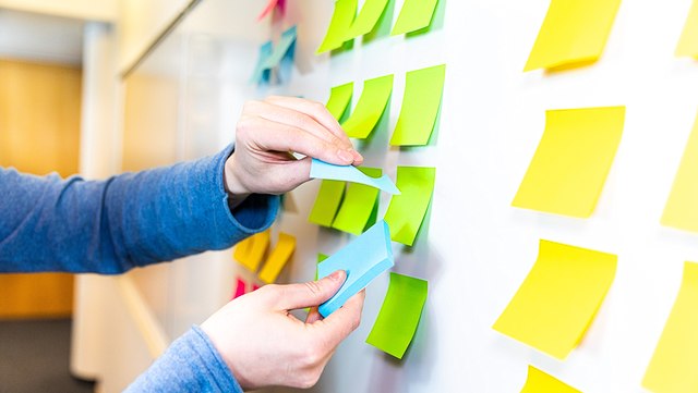 Eine Person klebt bunte Post-its auf eine Tafel