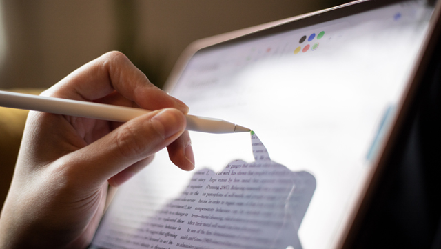 Nahaufnahme von einem Ipad. Eine Person hält den Pen in der Hand und klickt damit auf den Bildschirm